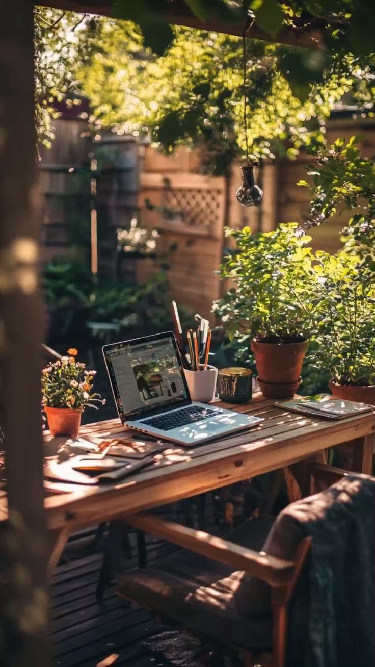 Mesa de madeira ao ar livre com laptop e plantas em um jardim ensolarado