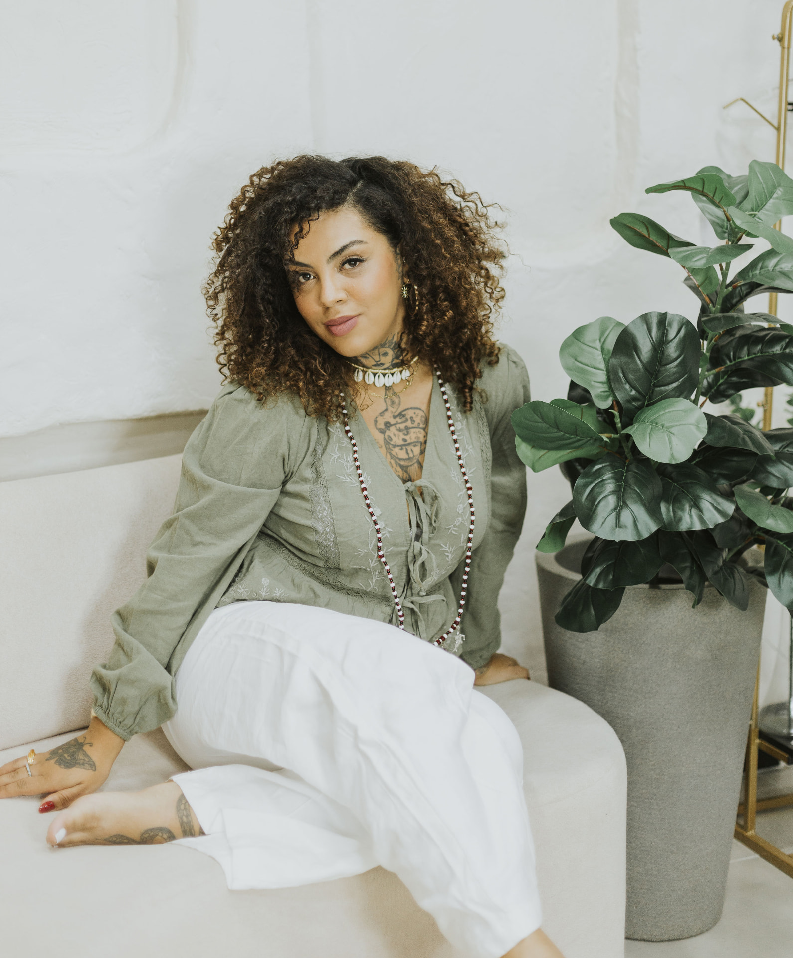 Kate Anne sentada em um sofá branco ao lado de uma planta
